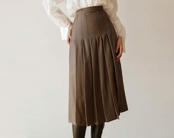 May include: A white long-sleeve blouse with a high collar and pleated front is paired with a brown pleated skirt. The skirt falls to mid-calf length. The outfit is a classic, elegant style.