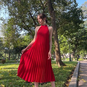 May include: A red halter dress with a pleated skirt. The dress is midi length and has a high neckline.