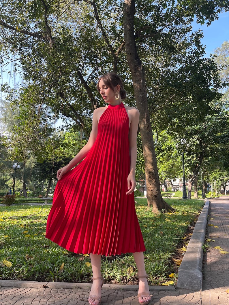 May include: A red halter dress with a pleated skirt. The dress is midi length and has a high neckline.
