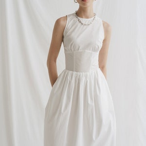 May include: A white sleeveless midi dress with a fitted bodice and a gathered skirt. The dress has a simple, elegant design.
