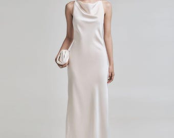 May include: A floor-length, ivory-colored satin dress with a cowl neckline and thin straps. The dress is paired with a matching clutch and white pointed-toe heels. The model is wearing silver earrings.