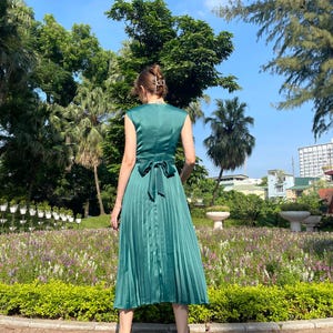 Peut inclure: Une robe midi pliss&eacute;e vert sarcelle avec un n&oelig;ud dans le dos. La robe est sans manches et a un col en V.