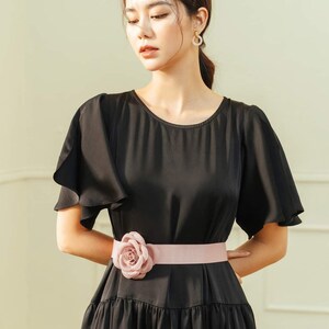 May include: A black dress with a ruffled neckline and short sleeves. The dress has a pink satin belt with a large pink flower accent.