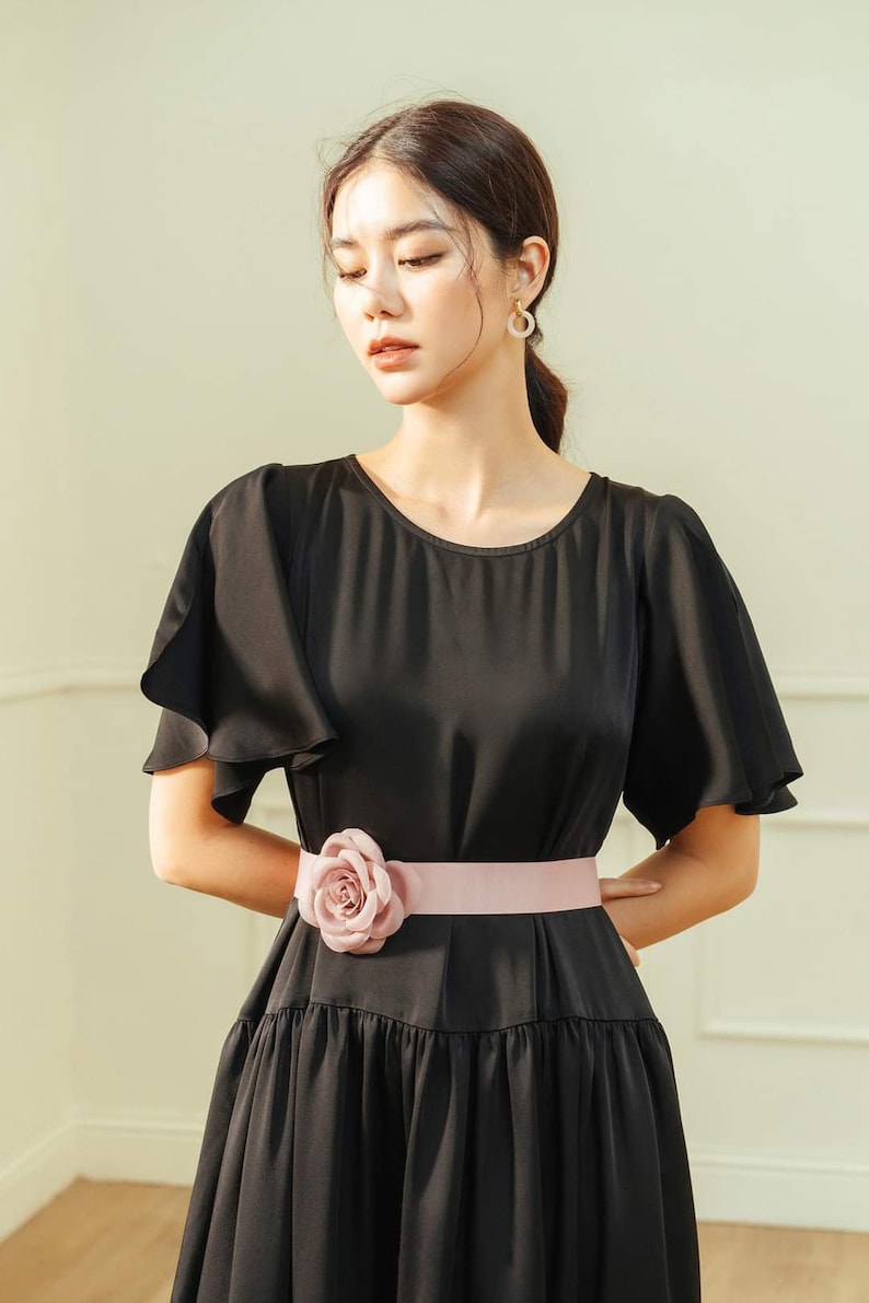 May include: A black dress with a ruffled neckline and short sleeves. The dress has a pink satin belt with a large pink flower accent.