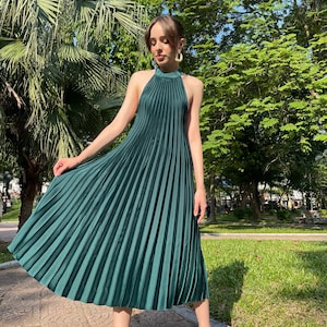 Pode incluir: Um vestido midi plissado verde escuro com decote halter. O vestido &eacute; sem mangas e tem uma silhueta fluida.