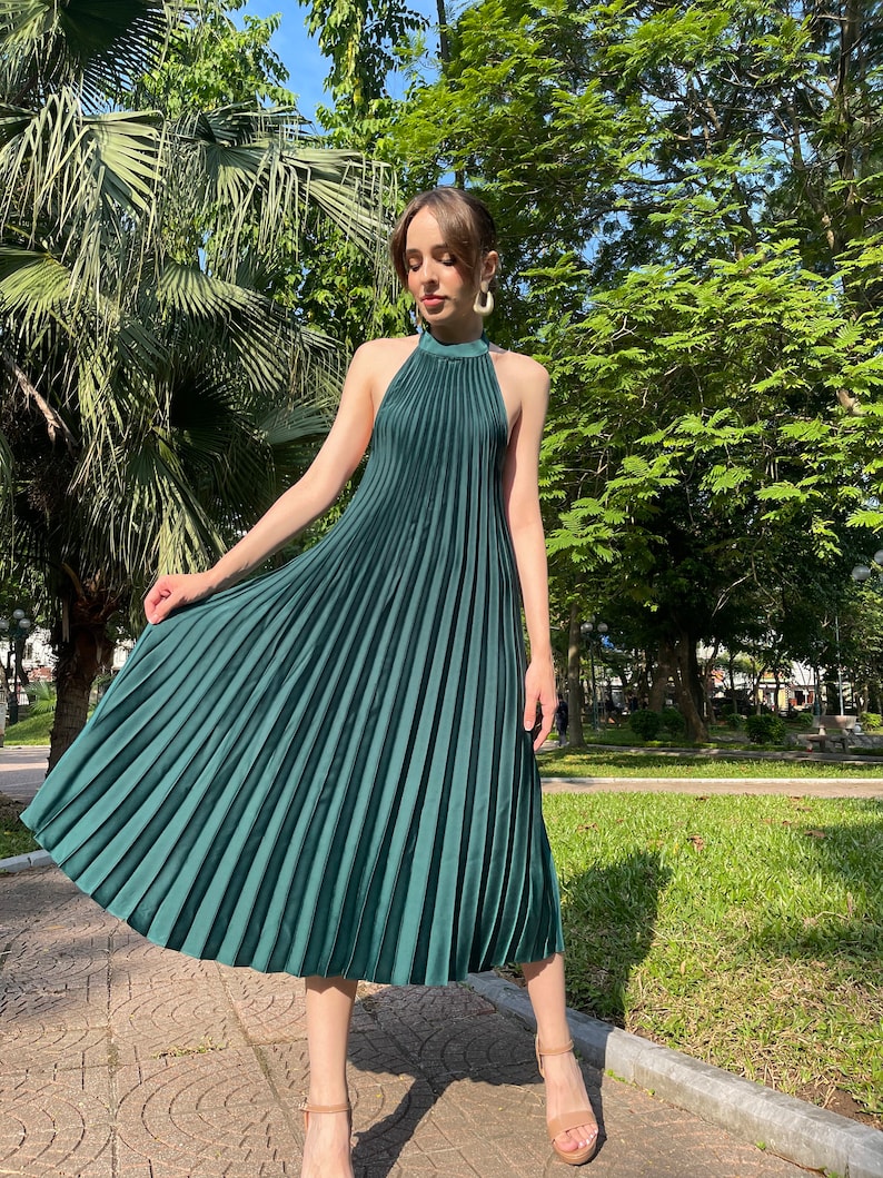 Pode incluir: Um vestido midi plissado verde escuro com decote halter. O vestido &eacute; sem mangas e tem uma silhueta fluida.