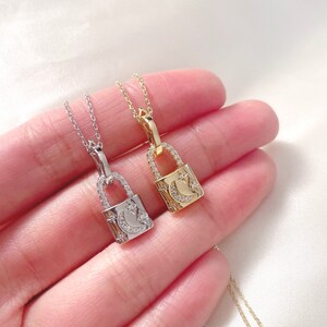 May include: Two delicate padlock pendant necklaces, one silver-toned and one gold-toned, each featuring a crescent moon and star design. The pendants are encrusted with small, sparkling stones and hang from fine chains.