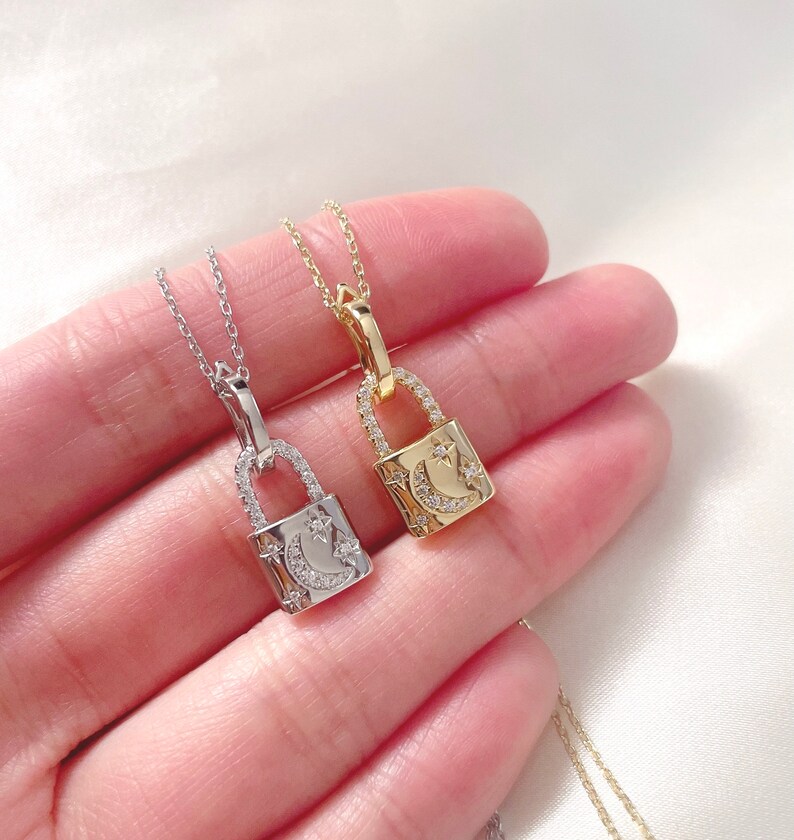 May include: Two delicate padlock pendant necklaces, one silver-toned and one gold-toned, each featuring a crescent moon and star design. The pendants are encrusted with small, sparkling stones and hang from fine chains.