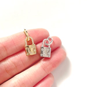 May include: Two small padlock pendants, one gold-toned and one silver-toned, each adorned with a crescent moon and star design. The pendants are embellished with small, sparkling crystals, adding a touch of elegance to the jewelry.