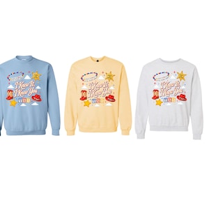 Op de afbeelding: Drie sweaters met ronde hals in lichtblauw, lichtgeel en heidegrijs. Elk heeft een afbeelding met de tekst "I Knew It I Knew You", een kralenarmband, een sheriffster, cowboylaarzen, een rode hoed en kleurrijke bouwblokken.