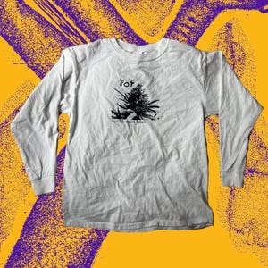 Pode incluir: Camiseta branca de manga comprida com gola redonda. A camiseta apresenta um gráfico preto de uma planta de cannabis, com a palavra "Pot" acima e o texto "zero G's always grown" abaixo. O fundo é amarelo e roxo.
