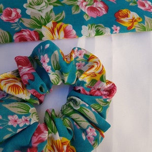 Pu&ograve; includere: Un elastico per capelli blu turchese con un motivo floreale con fiori rosa, gialli e bianchi.