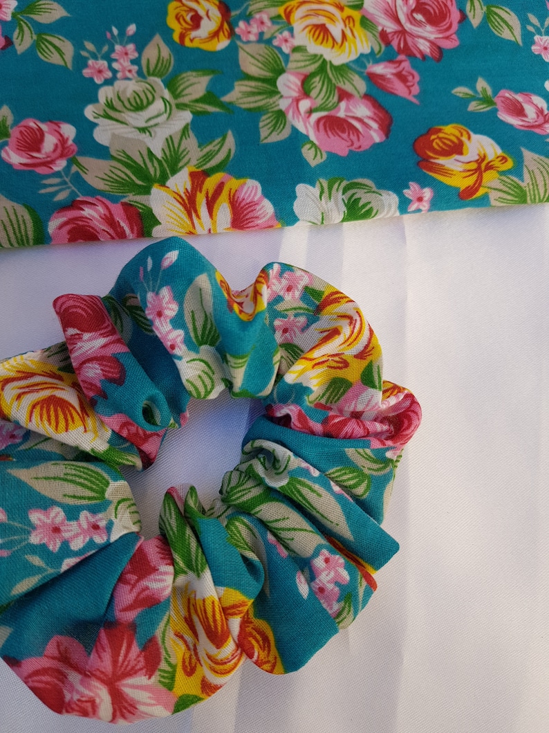 Pu&ograve; includere: Un elastico per capelli blu turchese con un motivo floreale con fiori rosa, gialli e bianchi.
