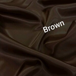 May include: A close-up of a smooth, brown fabric with a subtle sheen. The fabric is draped and folded, creating soft curves and folds. The word "Brown" is written in white text on the fabric.