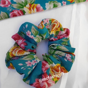 Pu&ograve; includere: Un elastico per capelli blu turchese con stampa floreale con fiori rosa, gialli e bianchi. L'elastico ha il testo "@mcfashion9" stampato su di esso.