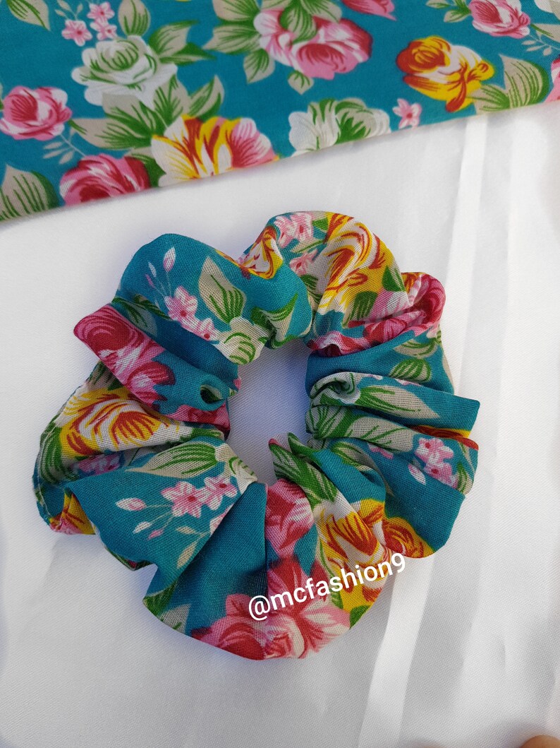 Pu&ograve; includere: Un elastico per capelli blu turchese con stampa floreale con fiori rosa, gialli e bianchi. L'elastico ha il testo "@mcfashion9" stampato su di esso.