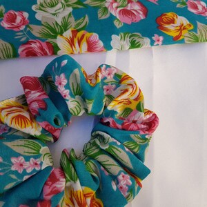 Pu&ograve; includere: Un elastico per capelli blu turchese con un motivo floreale con fiori rosa, gialli e bianchi.