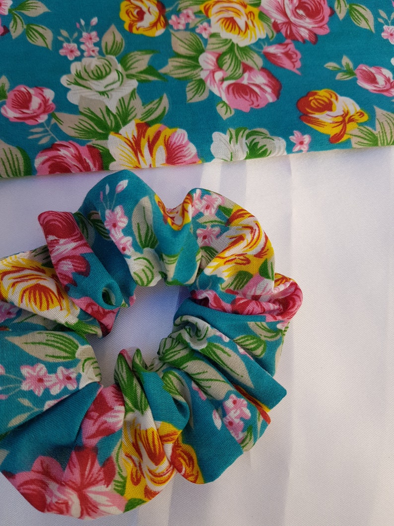 Pu&ograve; includere: Un elastico per capelli blu turchese con un motivo floreale con fiori rosa, gialli e bianchi.