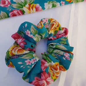 Pu&ograve; includere: Un elastico per capelli blu turchese con stampa floreale con fiori rosa, gialli e bianchi.