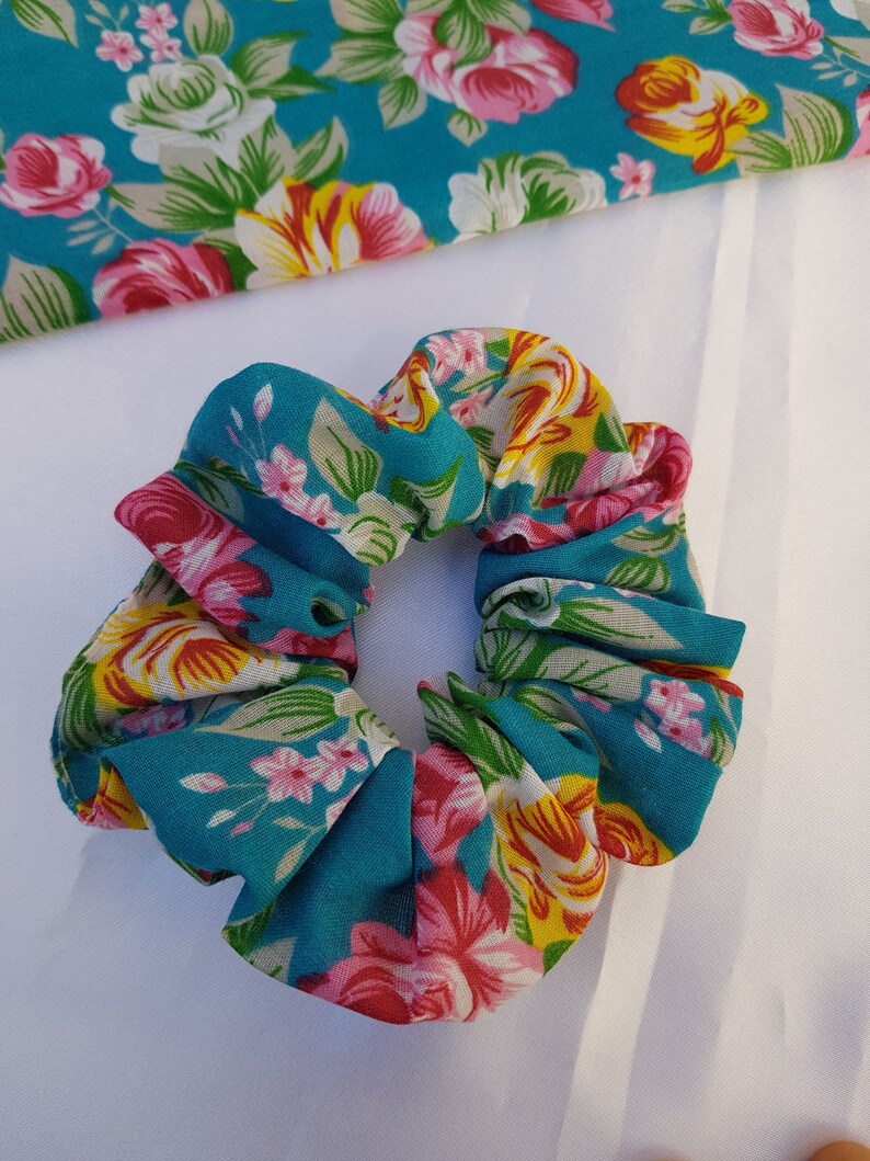 Pu&ograve; includere: Un elastico per capelli blu turchese con stampa floreale con fiori rosa, gialli e bianchi.