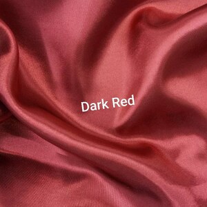 May include: Close-up of a smooth, dark red fabric. The fabric is folded and draped, creating soft folds and curves. The text "Dark Red" is printed in white on the fabric.