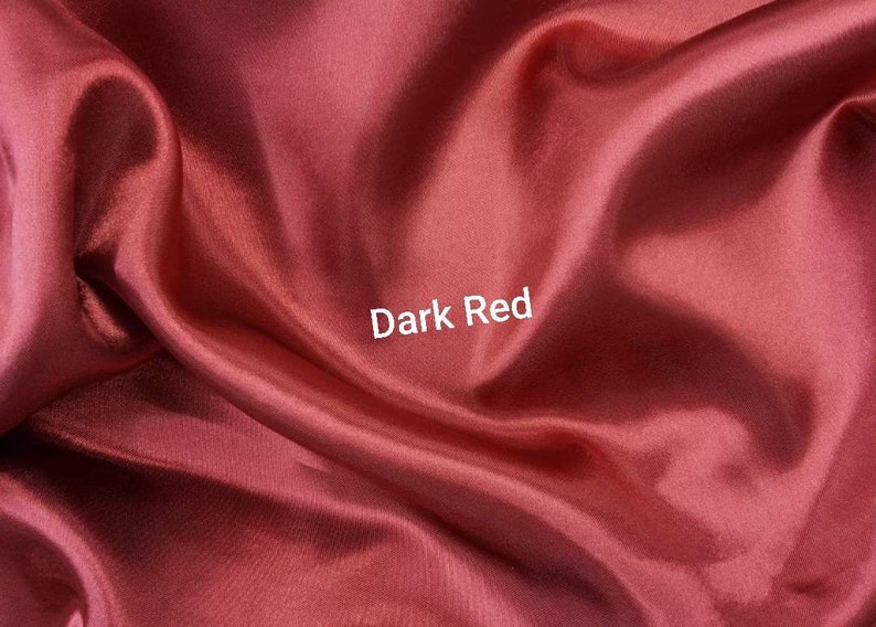 May include: Close-up of a smooth, dark red fabric. The fabric is folded and draped, creating soft folds and curves. The text "Dark Red" is printed in white on the fabric.