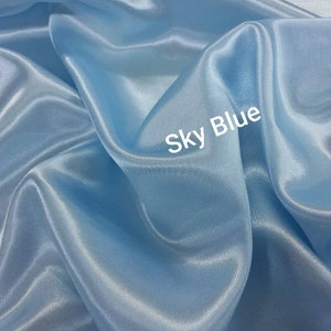 May include: A close-up of a smooth, light blue fabric with a subtle sheen. The fabric is draped and folded, creating soft curves and folds. The text "Sky Blue" is written in white on the fabric.