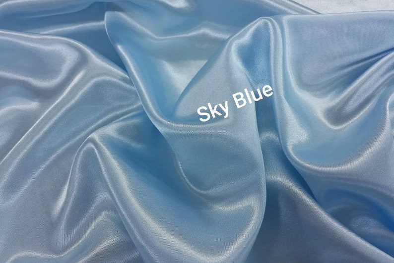 May include: A close-up of a smooth, light blue fabric with a subtle sheen. The fabric is draped and folded, creating soft curves and folds. The text "Sky Blue" is written in white on the fabric.