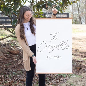 May include: A white canvas wall hanging with a wooden frame. The text "The Corzello Est. 2015" is printed in black cursive font.