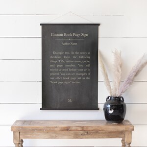 May include: Black and white custom book page sign with the text "Custom Book Page Sign" and "Author Name". The sign is hanging on a white wall above a wooden table with a black vase and dried flowers.