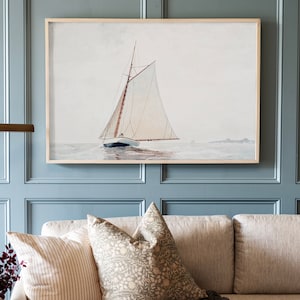 May include: A watercolor painting of a sailboat on the water. The sailboat has a white sail and a brown hull. The painting is framed in a light wood frame and is hanging on a light blue wall.