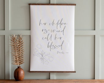May include: A white canvas wall hanging with a wood frame. The canvas features a floral design and the text "her children rise up and call her blessed Proverbs 31:28".