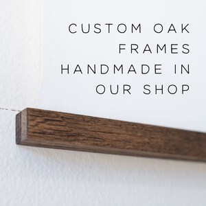 May include: A close-up of a dark brown wood frame with the text "CUSTOM OAK FRAMES HANDMADE IN OUR SHOP" printed on a white background.