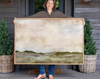 May include: A large rectangular landscape painting in a light wooden frame, featuring a soft watercolour-style depiction of rolling green hills under a muted, cloudy beige and cream sky, with visible textured canvas details throughout the artwork.