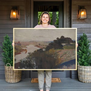 May include: A rectangular landscape painting in a gold frame featuring a river winding through a muted, earthy-toned countryside. The artwork includes cursive white text that reads: When you pass through the waters, I will be with you.