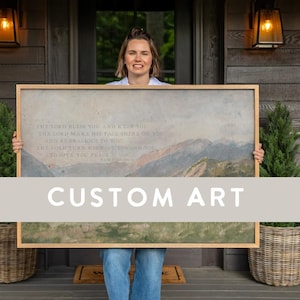 May include: A large rectangular framed wall art piece featuring a landscape painting of mountains under a cloudy sky. The artwork includes printed text that reads: The Lord bless you and keep you, the Lord make his face shine on you.