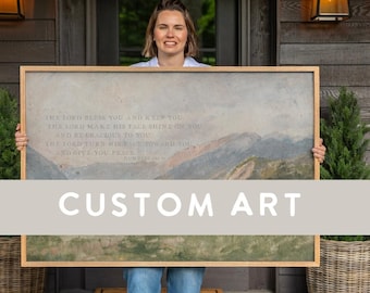 May include: A large rectangular framed wall art piece featuring a landscape painting of mountains under a cloudy sky. The artwork includes printed text that reads: The Lord bless you and keep you, the Lord make his face shine on you.
