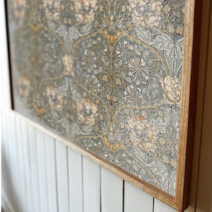Op de afbeelding: Een ingelijste print van een vintage bloemenpatroon in tinten groen, geel en wit. De print is in een natuurlijke houten lijst.