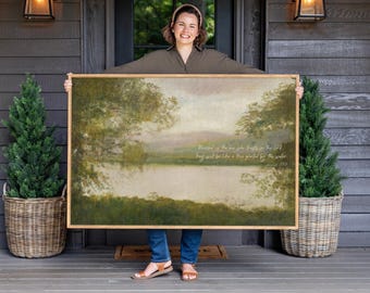 May include: A large rectangular framed wall art piece featuring a landscape painting of a calm lake surrounded by lush green trees and soft hills. The artwork includes white cursive text that reads, Blessed is the one who trusts in the Lord. They will be like a tree planted by the water.