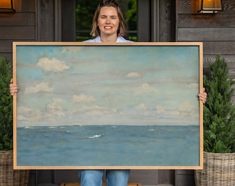 May include: A large rectangular landscape painting in a light wood frame depicting a calm blue ocean under a pale sky filled with soft white clouds. The artwork features horizontal bands of blue water and a light blue sky with scattered clouds.