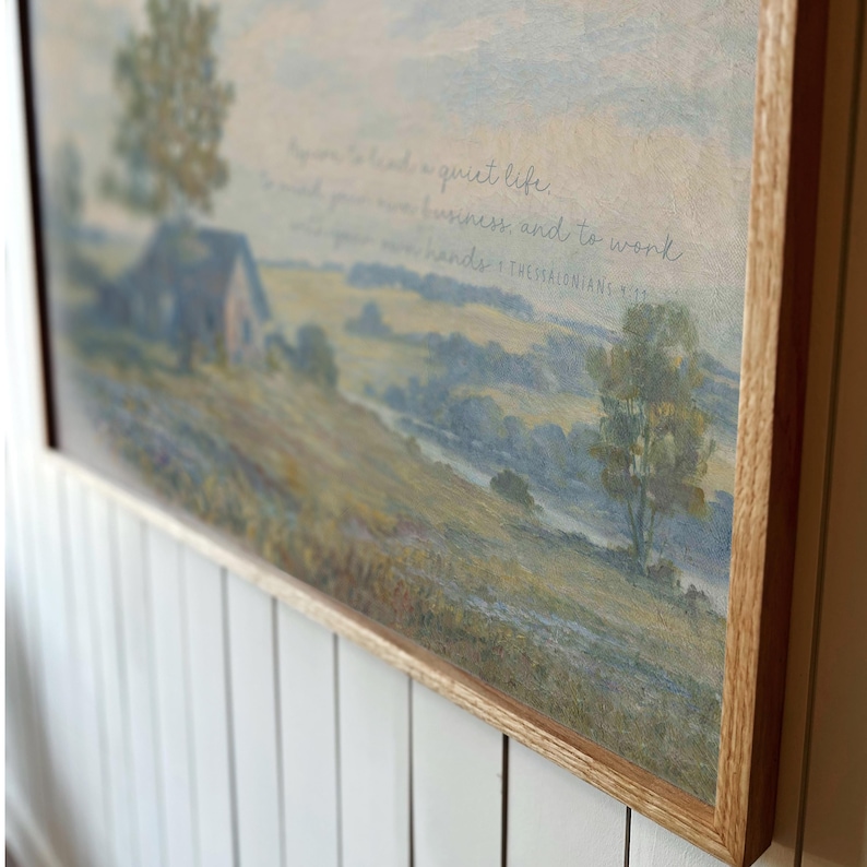 May include: Landscape painting in a light wood frame. The artwork depicts a rural scene with a house, trees, and a river. The painting has a soft, muted color palette with text that reads, "...to lead a quiet life..."