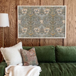 Op de afbeelding: Een groene fluwelen bank met twee kussens, een wit en een met een kleurrijk patroon. Een ingelijst schilderij met een bloemenpatroon hangt aan de muur achter de bank.
