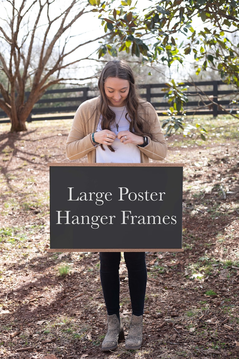 May include: A woman holds a black chalkboard sign with white text that reads "Large Poster Hanger Frames".