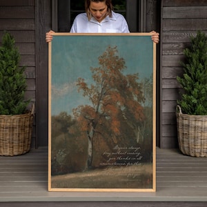 May include: A rectangular framed wall art print featuring a landscape painting of a large tree with orange and brown autumn foliage against a muted blue sky. The artwork includes cursive white text overlaid on the lower portion of the scene.