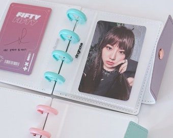 May include: White photo album with a light purple flap and a light green flap. The album has a clear plastic pocket on the front with a photo card inside. The photo card has a picture of a woman with long dark hair. The album has a ring binder with pink and blue rings. The album has the text "ringnote" printed on the side.