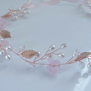 May include: A delicate floral hair accessory featuring a rose gold wire base adorned with faux pearls, pink crystal beads, and metallic gold leaves. A pale pink ribbon is attached for tying. This headpiece is suitable for weddings or special occasions.