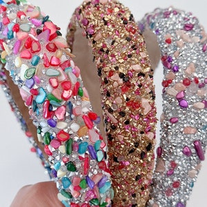 May include: Three headbands with different colored embellishments. The headband on the left has multi-colored stones, the middle headband has gold and pink stones, and the headband on the right has silver and pink stones.
