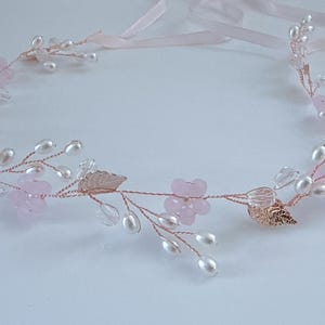 May include: A delicate floral headband featuring pink flowers, faux pearls, and rose gold leaves. The wired design includes clear crystal accents and pink ribbons for tying. This elegant headpiece is suitable for weddings or special occasions.