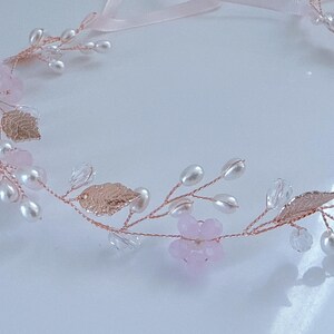 May include: A delicate floral hair accessory featuring a rose gold wire base adorned with pink flowers, faux pearls, clear crystals, and metallic gold leaves. A light pink ribbon is attached for tying. Perfect for weddings or special occasions.