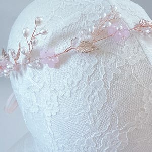 May include: A delicate floral hair crown featuring pink flowers, faux pearls, and gold-colored leaves. The crown is set on a thin, flexible wire, perfect for weddings or special occasions. The design is elegant and romantic.